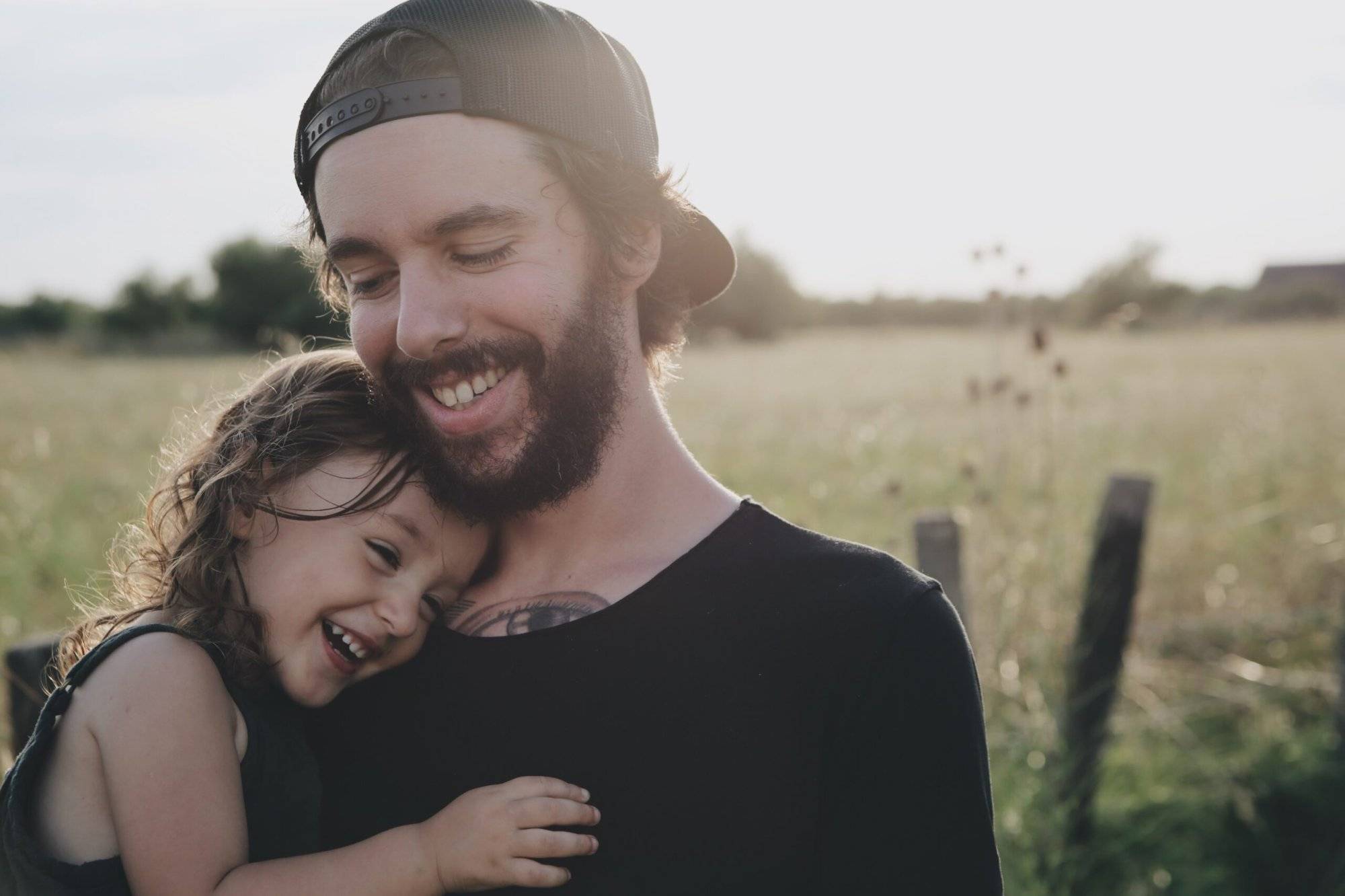 Father holding his little daughter, both smiling, with field of grass in distance